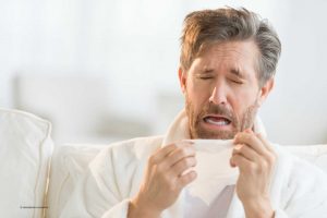 Mann mit Hyperhidrose und Erkältung niest und greift zum Taschentuch.